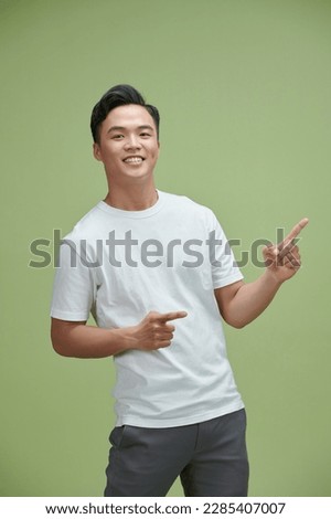Handsome healthy young Asian man smiling with his finger pointing isolated on light green 