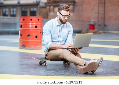 Handsome hipster businessman working with laptop sitting on the skateboard on the rooftop background. Lifestyle business concept - Powered by Shutterstock