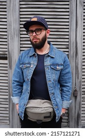 Handsome Hipster Guy In A Cap And Glasses With A Beard In A Blue Denim Jacket And A Fanny Pack.