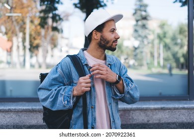 Handsome hipster guy in stylish white cap looking away during daytime sightseeing in city, Latino male tourist dressed in trendy clothing have solo vacations for exploring town during spring holidays