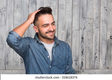 Handsome Hipster Man Combing His Thick Hair. Elegant And Stylish Man In Jeans Shirt Smiling And Looking Away Isolated On Wooden.