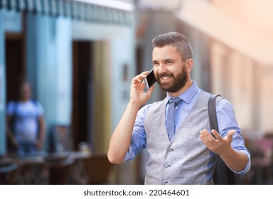 Handsome hipster modern businessman with beard walking in town and calling on mobile phone - Powered by Shutterstock