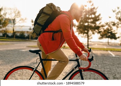 handsome hipster style bearded man in red hoodie and sunglasses riding alone with backpack on bicycle healthy active lifestyle traveler backpacker