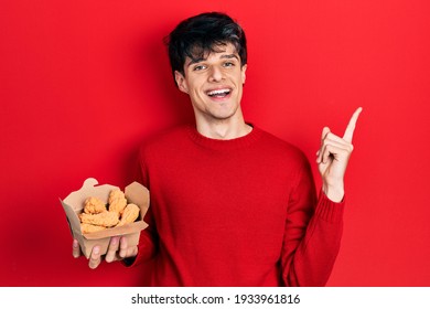 Handsome Hipster Young Man Eating Chicken Wings Smiling Happy Pointing With Hand And Finger To The Side 