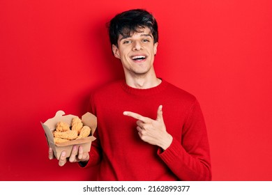 Handsome Hipster Young Man Eating Chicken Wings Smiling Happy Pointing With Hand And Finger 