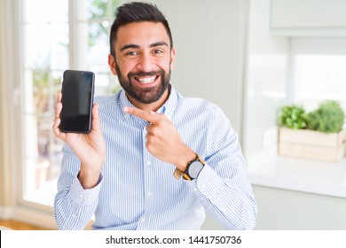 Handsome hispanic business man showing smartphone screen very happy pointing with hand and finger
