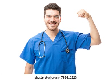 Handsome Hispanic doctor flexing his arm and showing his strength while wearing scrubs