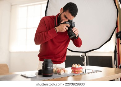 Handsome hispanic guy in casual professional photographer taking photo of tasty dessert cake and macarons, photo studio interior, young man holding digital camera, copy space - Powered by Shutterstock