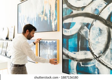 Handsome hispanic man adjusting a painting that is going to be on display in the new exhibiton of the art gallery
