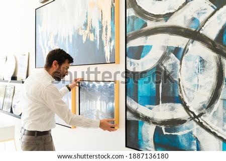 Handsome hispanic man adjusting a painting that is going to be on display in the new exhibiton of the art gallery