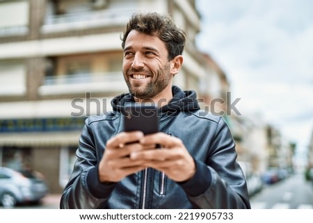 Handsome hispanic man with beard smiling happy outdoors using smartphone