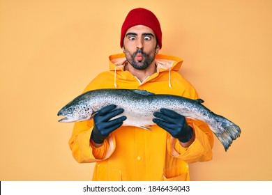 Handsome hispanic man with beard wearing fisherman equipment making fish face with mouth and squinting eyes, crazy and comical. 