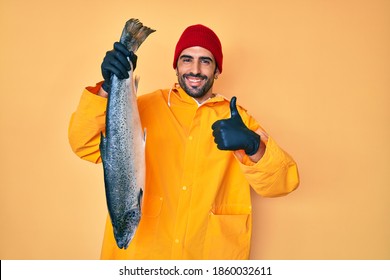 Handsome hispanic man with beard wearing fisherman equipment smiling happy and positive, thumb up doing excellent and approval sign 