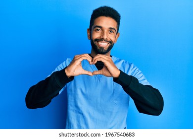 Handsome Hispanic Man With Beard Wearing Blue Male Nurse Uniform Smiling In Love Showing Heart Symbol And Shape With Hands. Romantic Concept. 