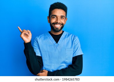 Handsome hispanic man with beard wearing blue male nurse uniform smiling happy pointing with hand and finger to the side 