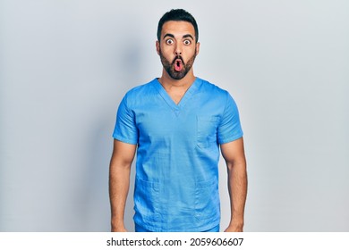 Handsome Hispanic Man With Beard Wearing Blue Male Nurse Uniform Afraid And Shocked With Surprise Expression, Fear And Excited Face. 