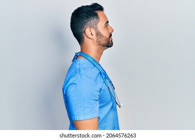 Handsome Hispanic Man With Beard Wearing Doctor Uniform Looking To Side, Relax Profile Pose With Natural Face With Confident Smile. 