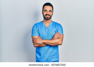 Handsome hispanic man with beard wearing blue male nurse uniform happy face smiling with crossed arms looking at the camera. positive person.  - Shutterstock ID 2076857503