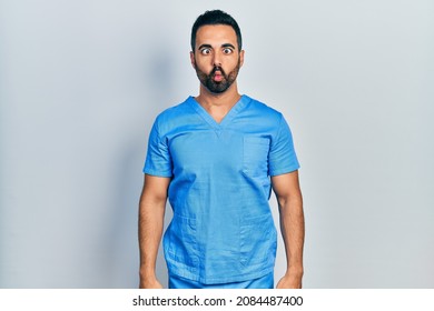 Handsome Hispanic Man With Beard Wearing Blue Male Nurse Uniform Making Fish Face With Lips, Crazy And Comical Gesture. Funny Expression. 