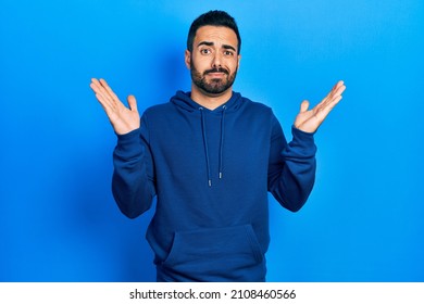 Handsome Hispanic Man With Beard Wearing Casual Sweatshirt Clueless And Confused With Open Arms, No Idea And Doubtful Face. 