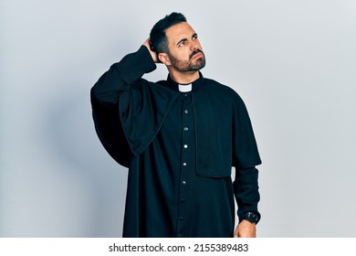 Handsome hispanic man with beard wearing catholic priest robe confuse and wondering about question. uncertain with doubt, thinking with hand on head. pensive concept. 