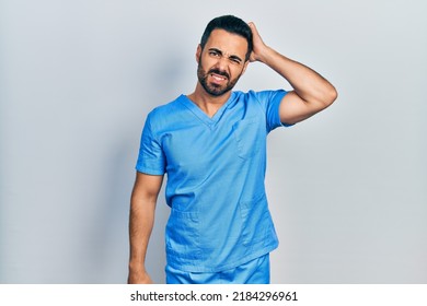 Handsome Hispanic Man With Beard Wearing Blue Male Nurse Uniform Confuse And Wonder About Question. Uncertain With Doubt, Thinking With Hand On Head. Pensive Concept. 