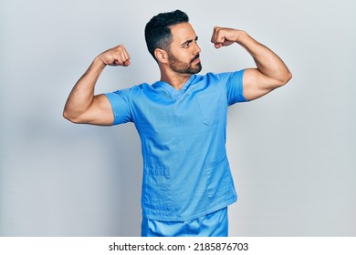 Handsome Hispanic Man With Beard Wearing Blue Male Nurse Uniform Showing Arms Muscles Smiling Proud. Fitness Concept. 