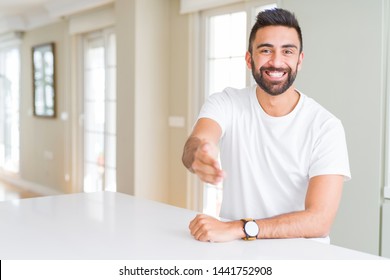 Handsome Hispanic Man Casual White T-shirt At Home Smiling Friendly Offering Handshake As Greeting And Welcoming. Successful Business.