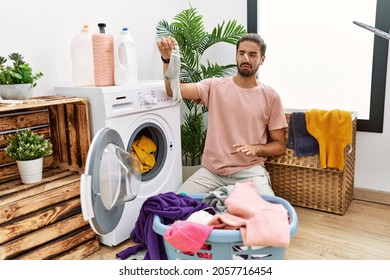 Handsome Hispanic Man Doing Laundry Covering Nose For Smelly Sock At Laundry Room