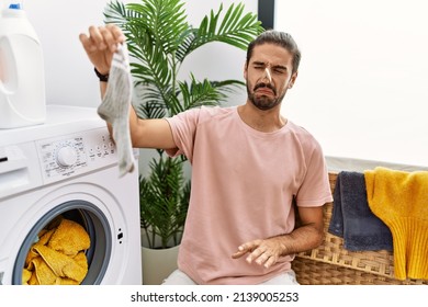 Handsome Hispanic Man Doing Laundry Covering Nose For Smelly Sock At Laundry Room