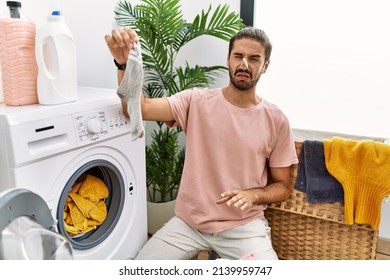 Handsome Hispanic Man Doing Laundry Covering Nose For Smelly Sock At Laundry Room