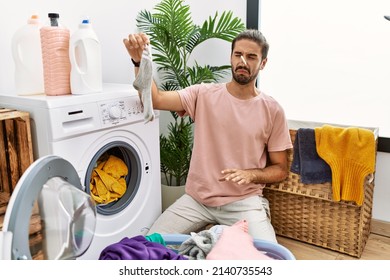 Handsome Hispanic Man Doing Laundry Covering Nose For Smelly Sock At Laundry Room