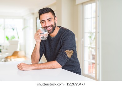 Handsome Hispanic Man Drinking A Fresh Glass Of Water With A Happy Face Standing And Smiling With A Confident Smile Showing Teeth