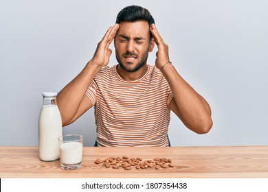 Handsome Hispanic Man Drinking Healthy Almond Milk With Hand On Head, Headache Because Stress. Suffering Migraine. 