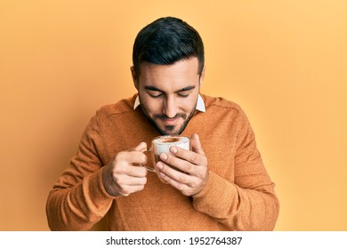 Handsome hispanic man enjoying a cup of coffee over yellow background - Powered by Shutterstock