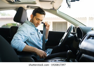 Handsome hispanic man in his 30s putting on her safety seatbelt before starting the car. Driver preparing to start working on a ride share app