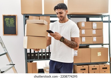 Handsome hispanic man holding cardboard boxes using smartphone at e-commerce store - Shutterstock ID 2208774295