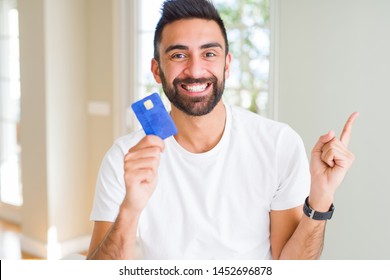 Handsome Hispanic Man Holding Credit Card Very Happy Pointing With Hand And Finger To The Side