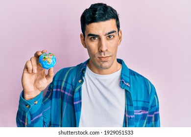 Handsome Hispanic Man Holding Small World Ball Thinking Attitude And Sober Expression Looking Self Confident 