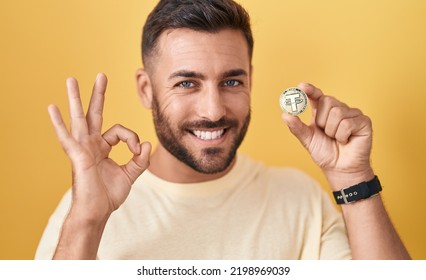 Handsome hispanic man holding tether cryptocurrency coin doing ok sign with fingers, smiling friendly gesturing excellent symbol  - Shutterstock ID 2198969039