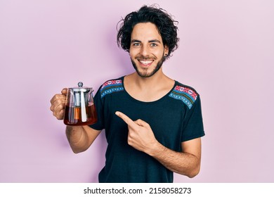 Handsome Hispanic Man Holding Traditional Tea Pot Smiling Happy Pointing With Hand And Finger 