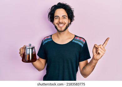 Handsome Hispanic Man Holding Traditional Tea Pot Smiling Happy Pointing With Hand And Finger To The Side 