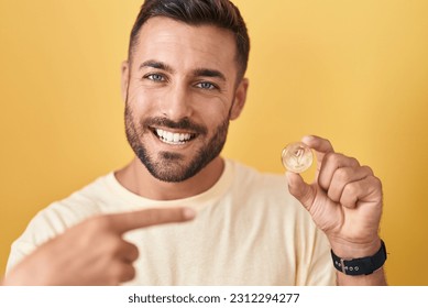 Handsome hispanic man holding tron cryptocurrency coin smiling happy pointing with hand and finger 