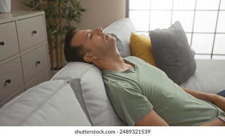 Handsome hispanic man relaxing on a couch in a living room of his home, wearing a green shirt and leaning back with closed eyes. - Powered by Shutterstock