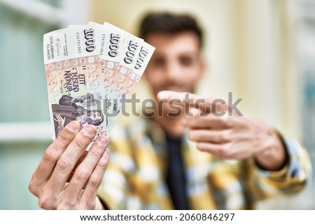 Handsome hispanic man smiling happy and confident at the city holding 1000 iceland krona banknotes