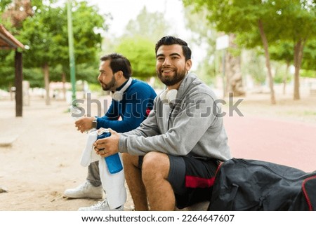 Handsome hispanic man smiling while getting ready to go for a run or exercise with a friend at the park