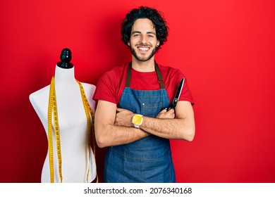Handsome hispanic man standing by manikin holding scissors smiling with a happy and cool smile on face. showing teeth. 