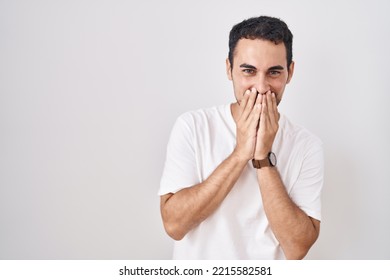 Handsome Hispanic Man Standing Over White Background Laughing And Embarrassed Giggle Covering Mouth With Hands, Gossip And Scandal Concept 