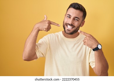 Handsome hispanic man standing over yellow background smiling cheerful showing and pointing with fingers teeth and mouth. dental health concept.  - Shutterstock ID 2222370455