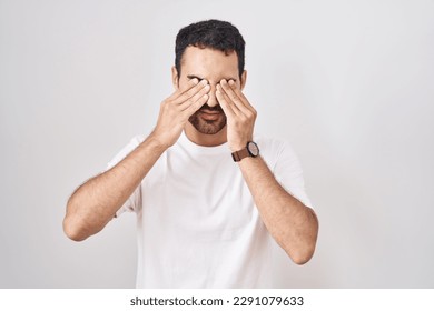 Handsome hispanic man standing over white background rubbing eyes for fatigue and headache, sleepy and tired expression. vision problem  - Powered by Shutterstock